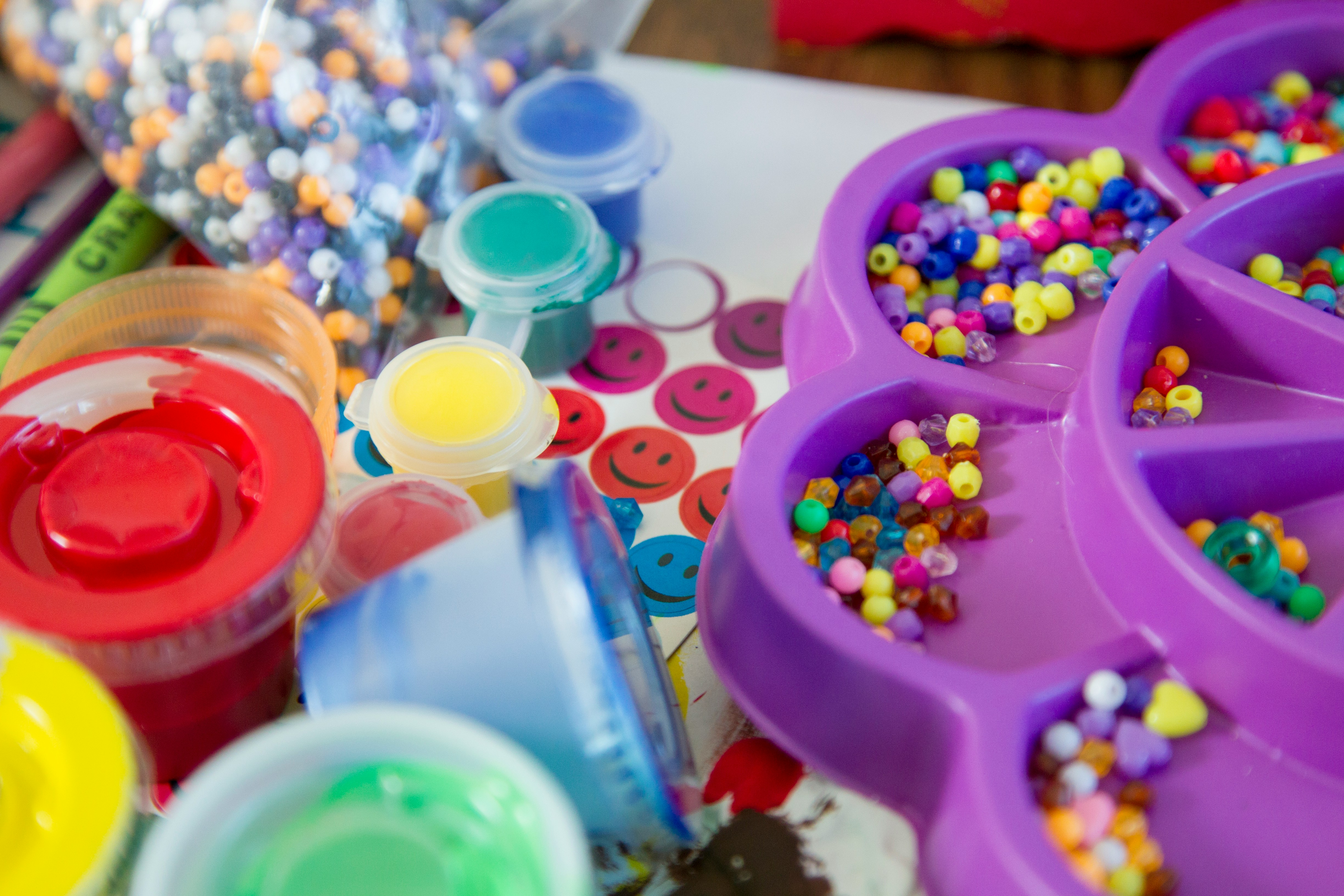 Colorful art supplies including paint, brushes, and beads organized in various containers on a table.