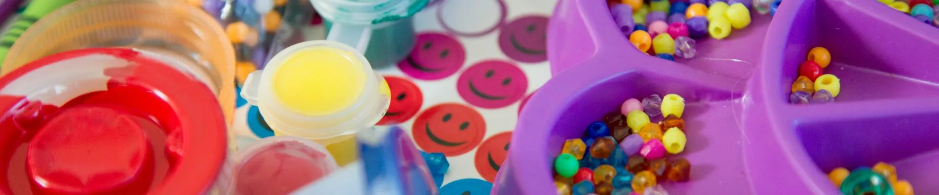 Colorful art supplies including paint, brushes, and beads organized in various containers on a table.