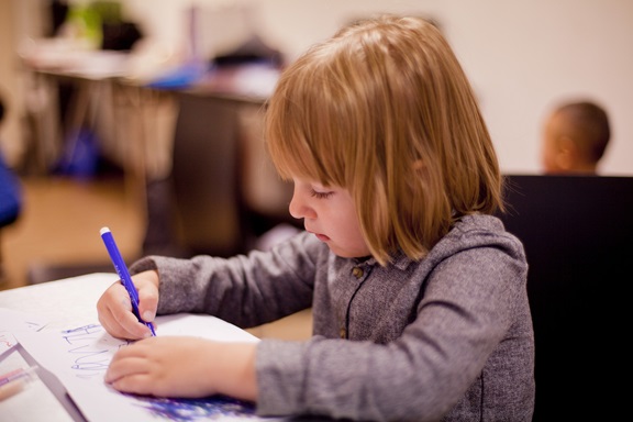 A young child writing sitting at a desk