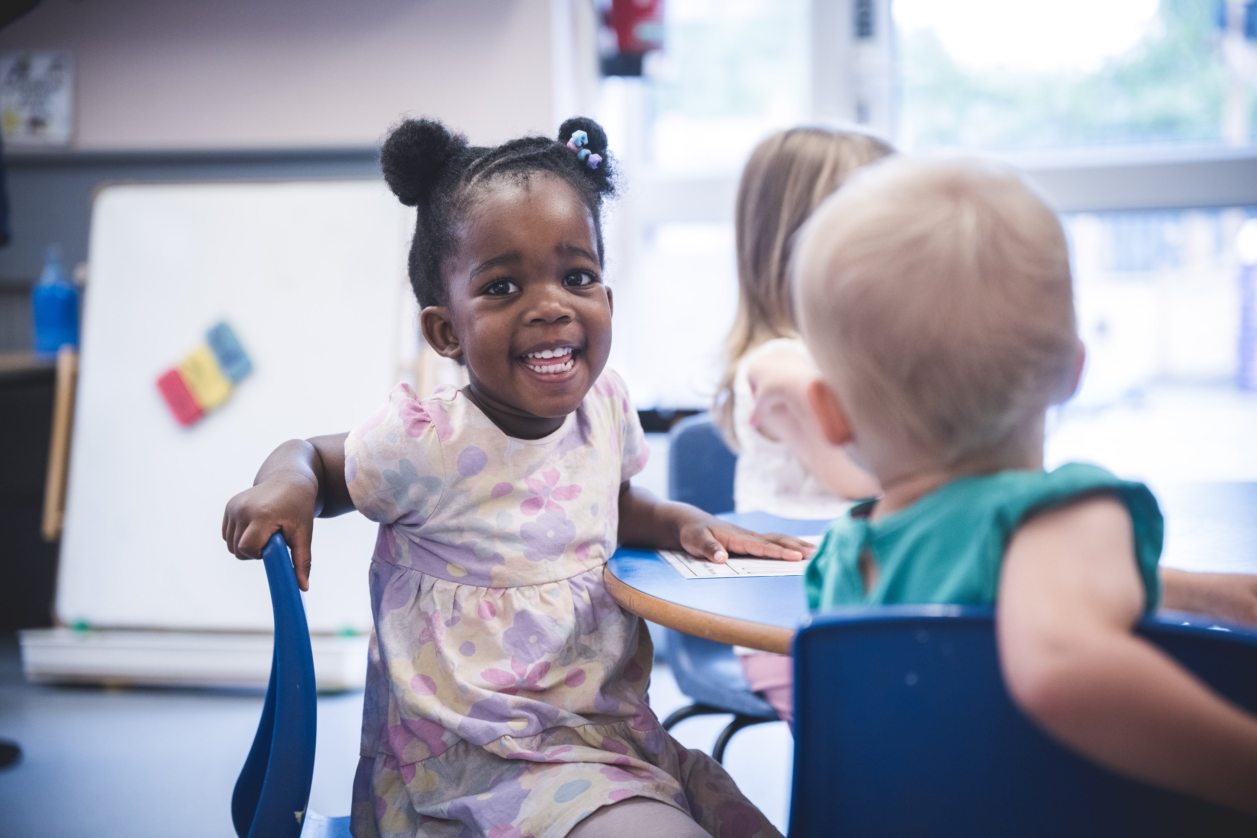 3 young children sat at a round table in a nursery setting