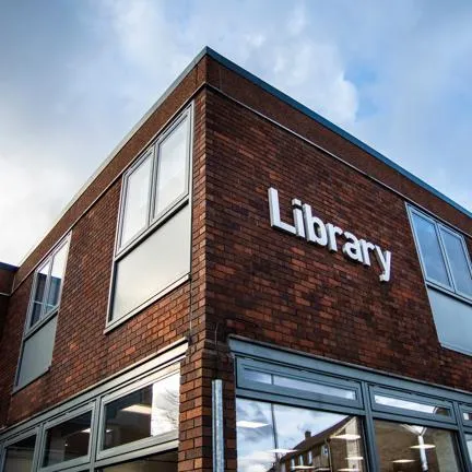 A photo of outside Arnold Library showing the white library sign in front of the orange bricked building.