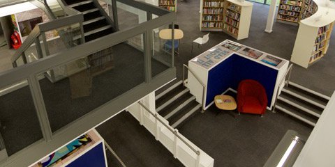 Inside of Arnold library from a mezzanine,  showing stairs, shelves with books and cosy chairs.