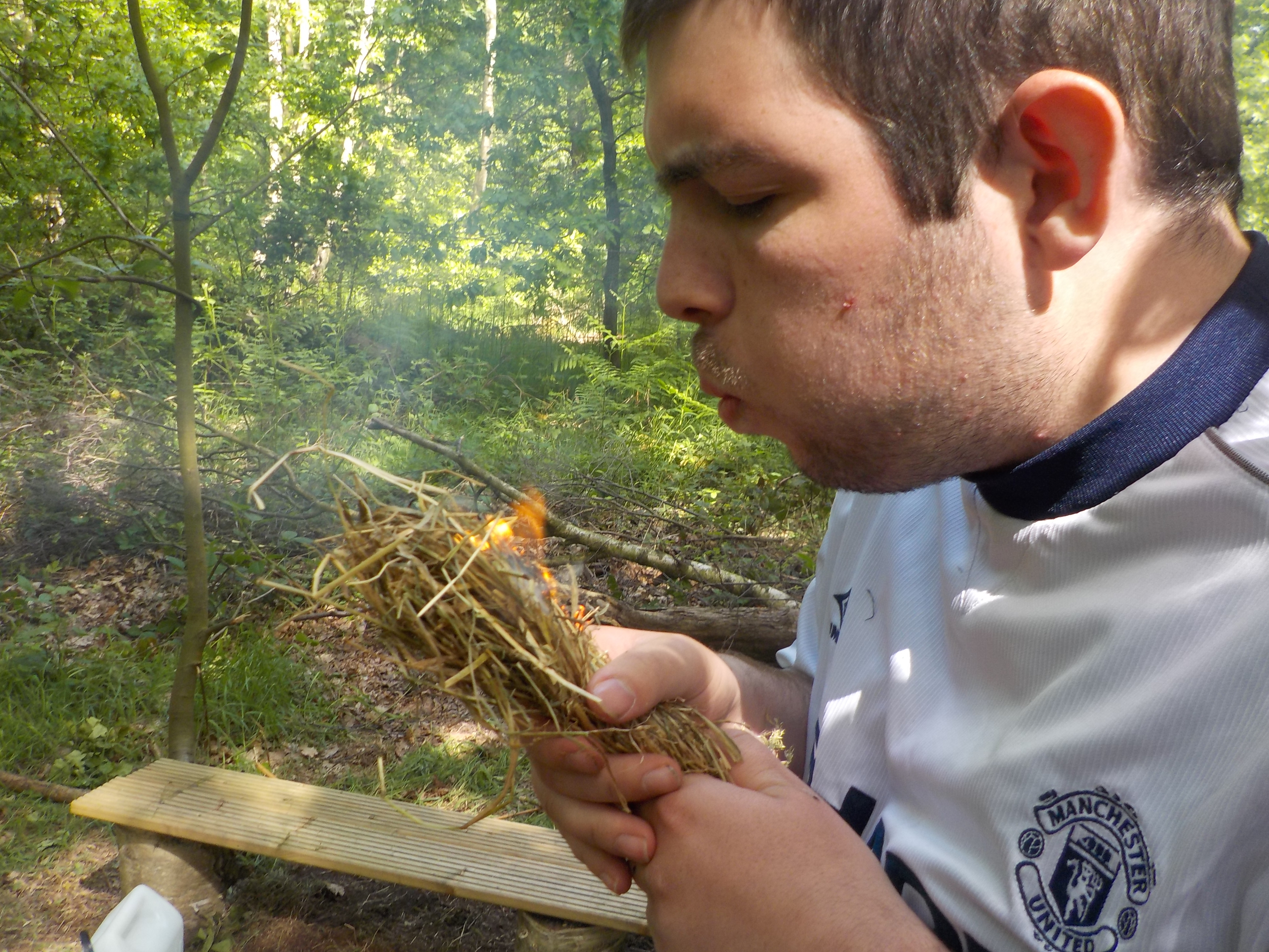 Young man blowing kindling to make fire