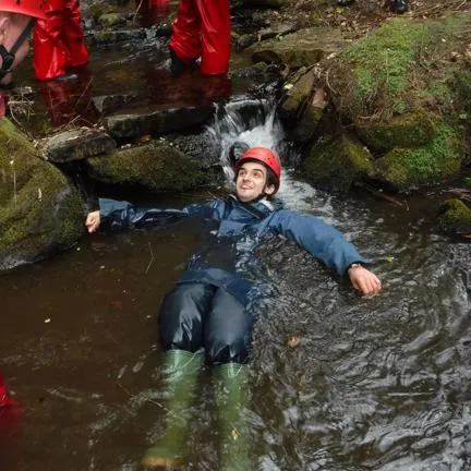 Man in caving equipment lying in a stream