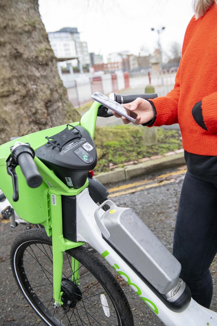 Person standing next to green e-bike holding phone