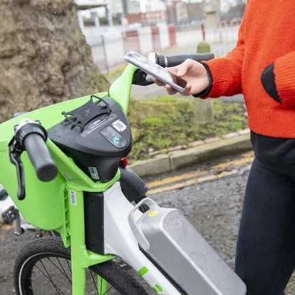 Person standing next to green e-bike holding phone