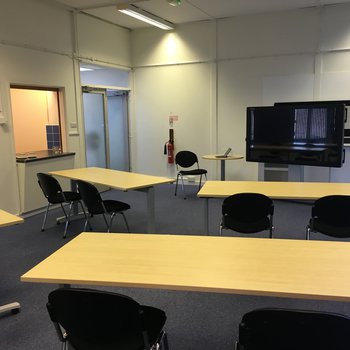 Interior shot of meeting room 
wooden desks with chairs and a monitor on the far wall