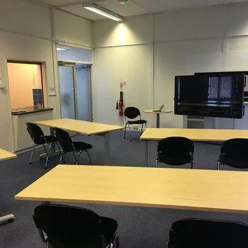 Interior shot of meeting room
wooden desks with chairs and a monitor on the far wall