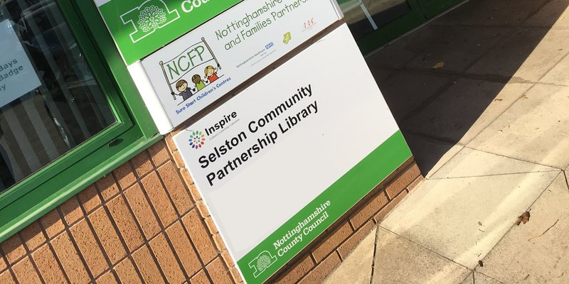 Green and white entrance sign outside Selston Library.