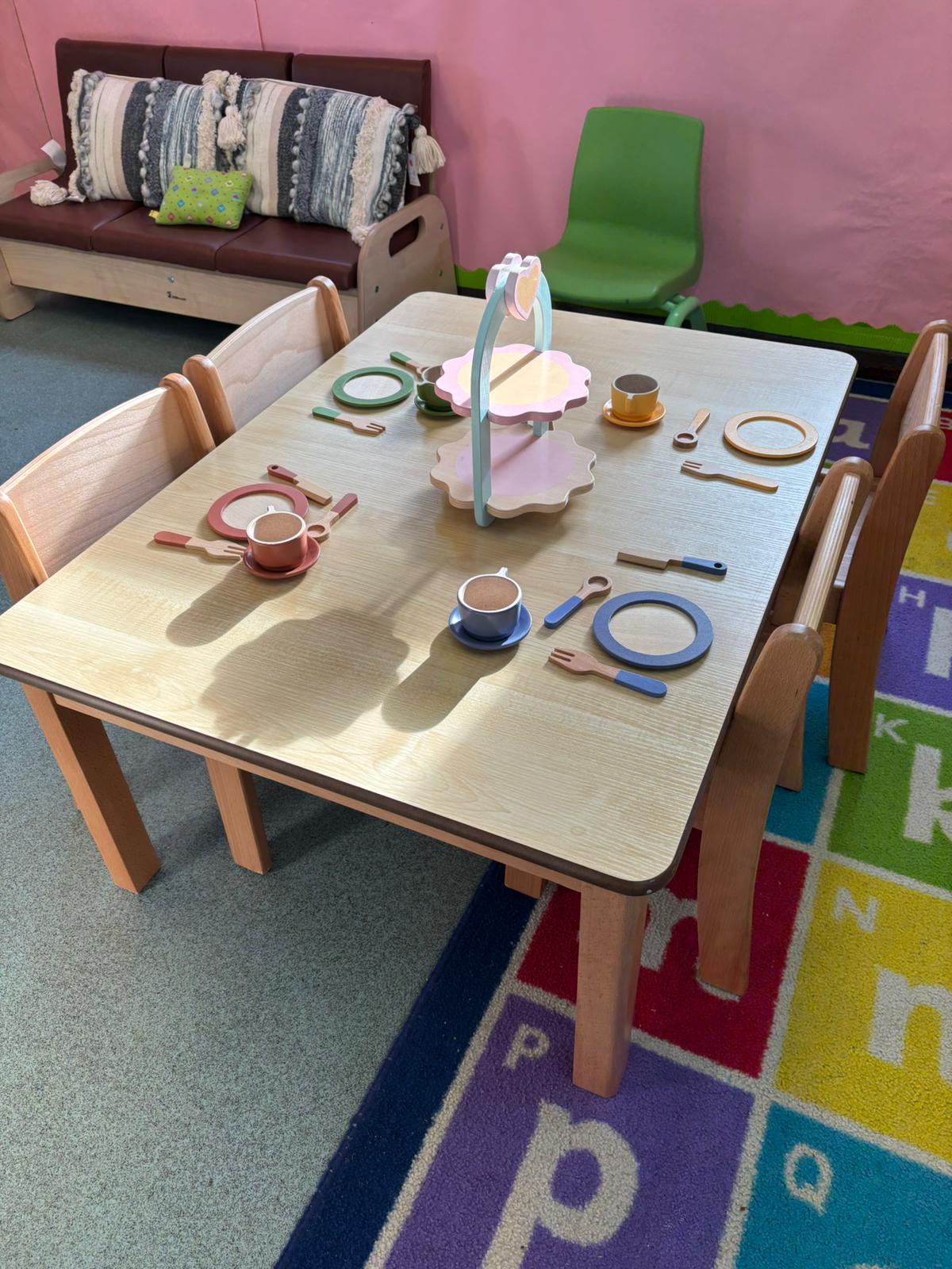 A low level natural wood table and chairs with wooden crockery and cutlery set up, part of a home corner activity